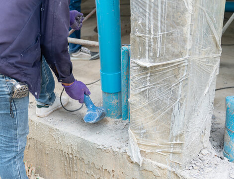 Plumber wearing purple safety gloves using an electric heat gun to warm and soften a blue PVC pipe joint at a construction site.