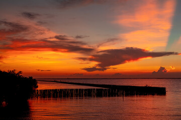 Fototapeta premium Dramatic sunset sky above the tropical ocean with glowing orange clouds, radiant crepuscular rays, calm water reflections and scenic coastal horizon during a peaceful evening. Nature background.