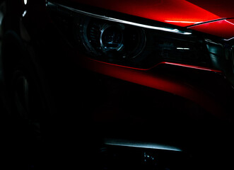Closeup headlight of shiny red luxury SUV compact car. Elegant electric car technology and business concept. Hybrid auto and automotive concept. Car parked in showroom or motor show. Car dealership. © Fahroni