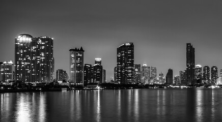 Fototapeta premium Black and white Bangkok skyline at night along Chao Phraya River in Thailand. Illuminated skyscrapers, waterfront reflections and timeless monochrome urban architecture. Night cityscape in Thailand.