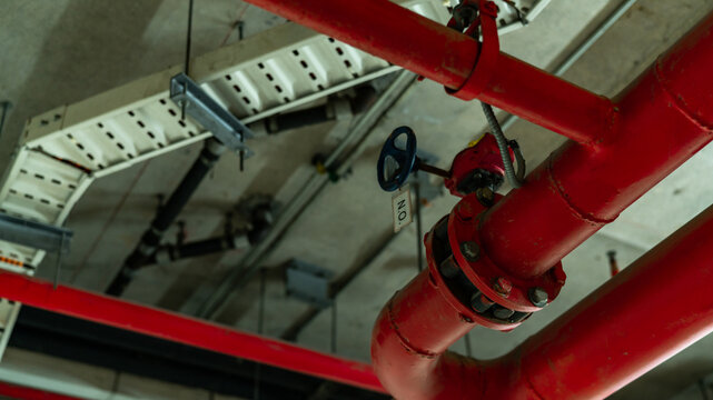 Red fire protection sprinkler piping network suspended from a modern building ceiling, featuring industrial engineering, fire suppression equipment, safety infrastructure and mechanical installation.