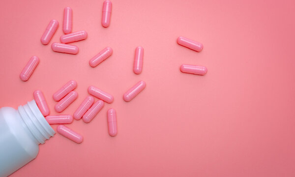 Pink capsule spread out of white plastic drug bottle. Capsule and pill bottle on pink background. Vitamins and supplements for healthy skin, collagen boost, and acne treatment concept. Online pharmacy