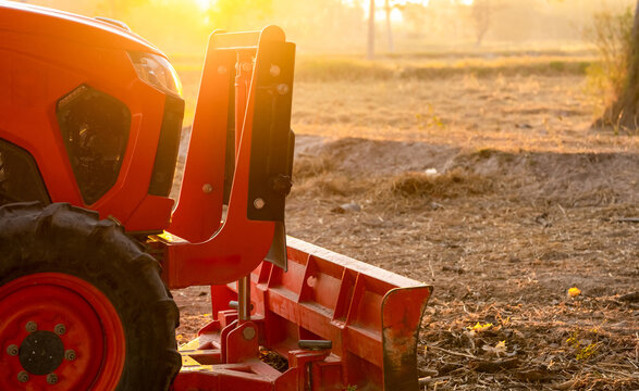 Orange tractor parked at rice farm in summer morning with sunlight. Agricultural machinery in agriculture farm. Smart farming concept. Vehicle in farm. Labor saving machinery. Equipment for plantation