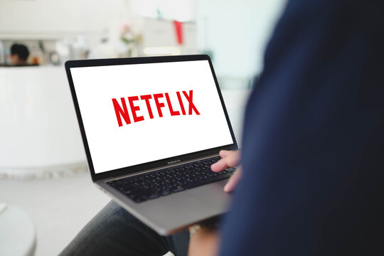 Bangkok, Thailand. July 24, 2026; An over the shoulder view of a person holding a MacBook Pro laptop displaying the Netflix logo on a white screen.