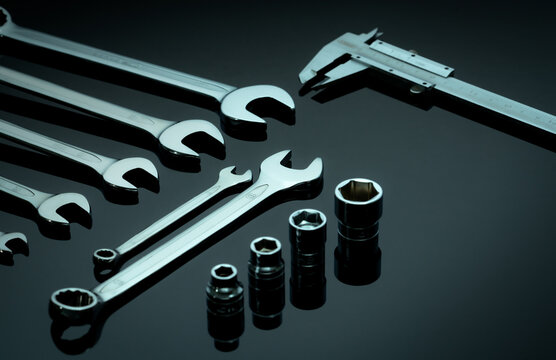 Set of chrome wrenches or spanners, hexagon socket, and vernier caliper on dark table in workshop. Chrome vanadium spanner wrench. Silver wrenches. Mechanic tools. Hardware for service technician.