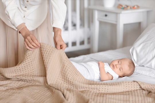 Muslim mother covering her sleeping baby with blanket on bed at home, closeup