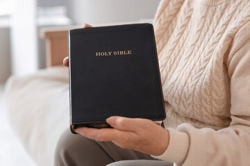 Obraz premium Senior woman with Bible sitting on sofa at home, closeup