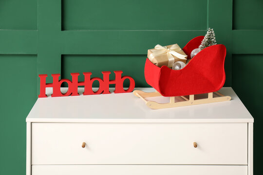 Beautiful Christmas decor and gift box on chest of drawers against color wall