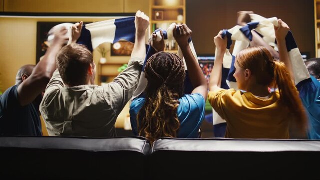 Happy soccer supporters clink beer cups after a positive match result while excited football supporters drink alcohol and react on the couch.