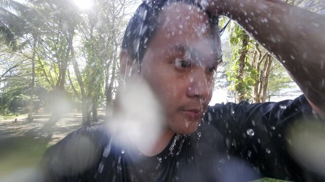 Dressed asian man taking an outdoor shower. Close up shot