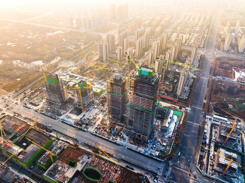 Aerial shot of an active urban construction site with multiple high-rise buildings under construction, cranes and surrounding city infrastructure.