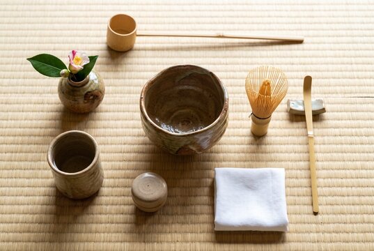 畳の上に丁寧に配置された茶碗、茶筅、茶杓、柄杓、茶入、布巾、そして一輪の花。和室に広がる静けさと自然光が、茶の湯の美しさと心を整える時間を伝える一枚