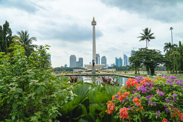 Obraz premium Jakarta, Indonesia - July 24, 2026: The National Monument (Monas) rises above landscaped gardens and colorful flowers at Merdeka Square, with Jakarta's skyline in the background.