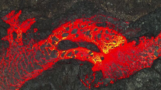 Molten lava flows across dark volcanic rock in dynamic aerial view