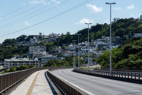 快晴の空と正面の斜面に住宅地のある橋の点字ブロックが続く歩道と車道