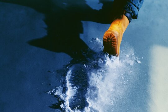 Close up of a winter boot treading into crisp deep snow, creating a detailed footprint in a moody teal setting for footwear and hiking themes