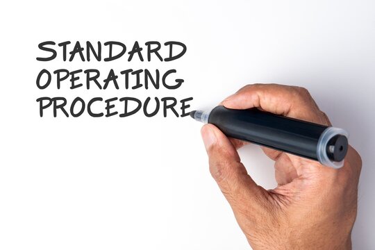 Hand holding a black marker writing the phrase Standard Operating Procedure on a white background. Corporate guidelines, business workflows, organizational rules, regulatory compliance concept.