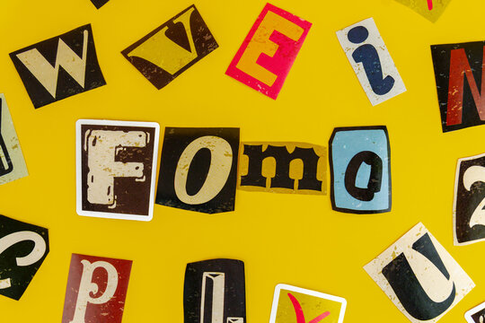 Ransom note style cutout letters spelling the acronym FOMO on a yellow background. Fear of missing out, consumer psychology, marketing urgency, social media anxiety concept.
