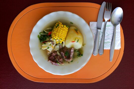 Traditional South American soup dish with corn on the cob served in a white bowl