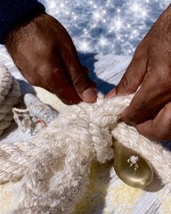 Fototapeta premium Close up of hands tying a manila rope knot on a brass cleat at a sunlit wooden pier for nautical craft and maritime style concepts
