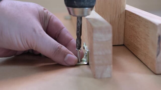 4K video of fastening a metal corner bracket to wooden furniture using a power screwdriver. For furniture assembly, DIY, woodworking, and home improvement concepts