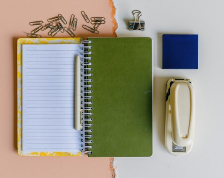Open notebook with sage green cover and blank ruled pages on a split background with a pen, stapler and paperclips for office organization and study