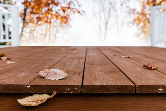 Rustic wooden table with weathered planks and fallen dry leaves over a blurred autumn park background for seasonal product display