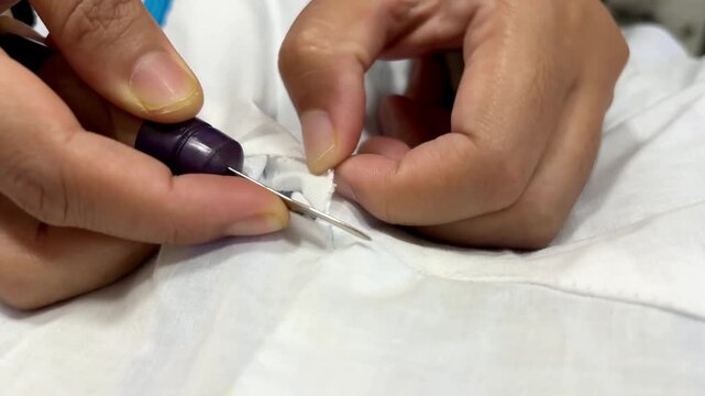 Close up of an Asian female tailor unpicking stitches on fabric using a seam ripper tool