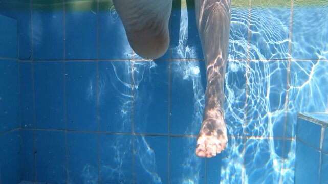 Slow motion underwater video of a girl dangles her feet in the pool water.