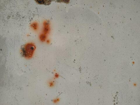 A light-colored painted metallic panel showing distinct orange rust spots and subtle surface scratches throughout