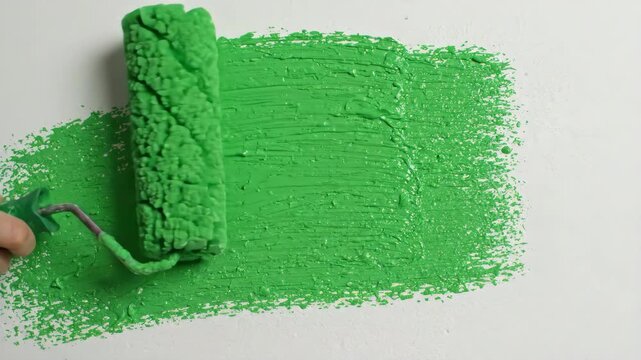 Close up shot of a foam paint roller applying bright green paint onto a smooth wall creating a solid green screen surface for chroma key