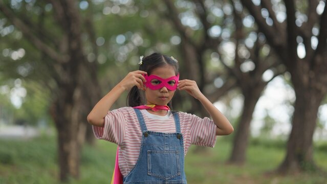 Active Asian little kids pretending to be superheroes playing together outdoors in nature park. Children roleplay, imaginative fantasy, and brave hero childhood lifestyle.