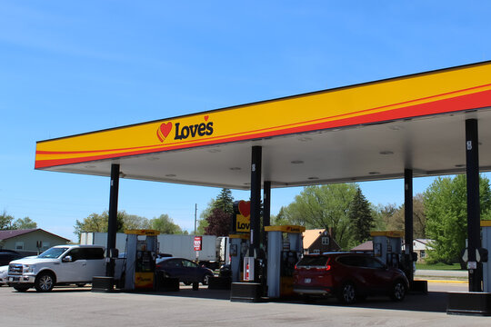 A Love's Travel Stop gas station canopy with fueling pumps and cars under a bright blue sky (Oakdale, WI - May 14, 2026)