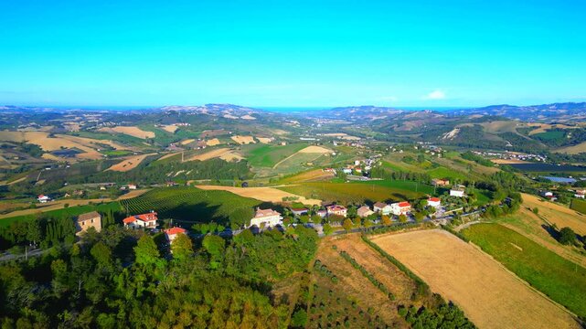Serene aerial truck left pan right shot from Monte Rinaldo, capturing vast expanses from the heights, filled with meadows, fields, roads, buildings, trees, reaching up to distant hillscapes, mountains
