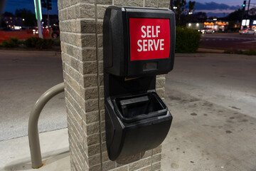 Horizontal view of a self-serve windshield cleaning station at a gas station, featuring a squeegee and cleaning fluid container against a brick wall © Juli