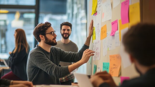 Professional man places a sticky note on a white board while his colleagues observe the project progress in the office.