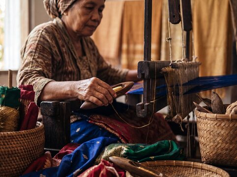Sumatran woman weaving Songket fabric on a traditional wooden loom.