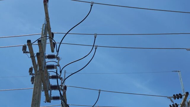 Pan right video of disconnect switches and T-clamps connecting jumper wires on a high voltage concrete pole, industrial electrical power grid infrastructure under blue sky.