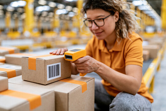 Warehouse worker scanning package with handheld barcode reader in distribution warehouse, woman checking parcel for shipping and inventory