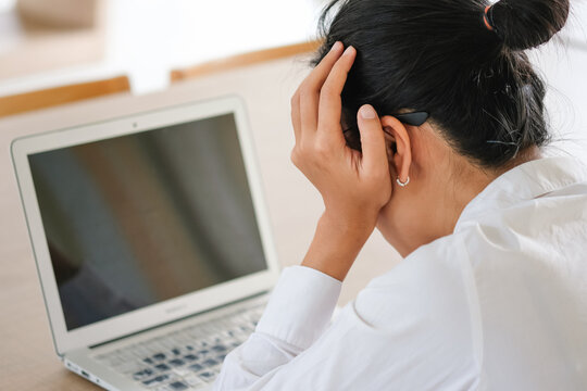 A stressed woman holding her head in her hands while working on a laptop, depicting workplace pressure, burnout, frustration, and the mental strain of modern employment. concept health care