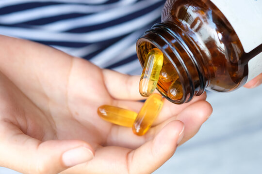 Hand of woman yellow gel capsules being poured from a supplement bottle into a person's hand, representing health, daily nutrition, and wellness routines.concept health care