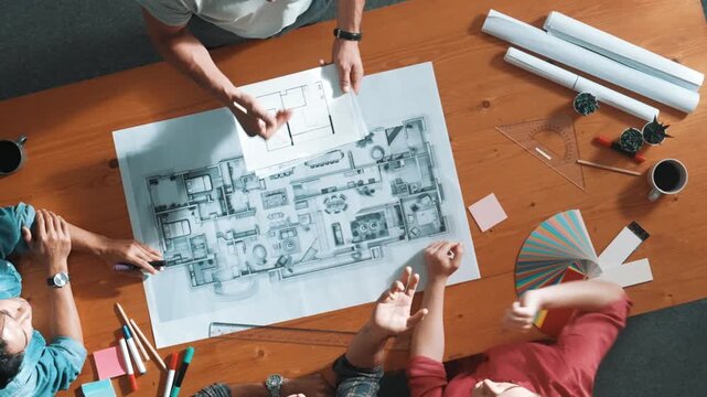 Top down view of manager looking at document while team planing building. Aerial view of skilled architect engineer holding and send blueprint at meeting table project plan and blueprint. Symposium.