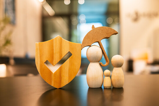 Wooden shield check mark umbrella family figure real estate insurance property protection home safety agent broker healthcare guarantee security concept.