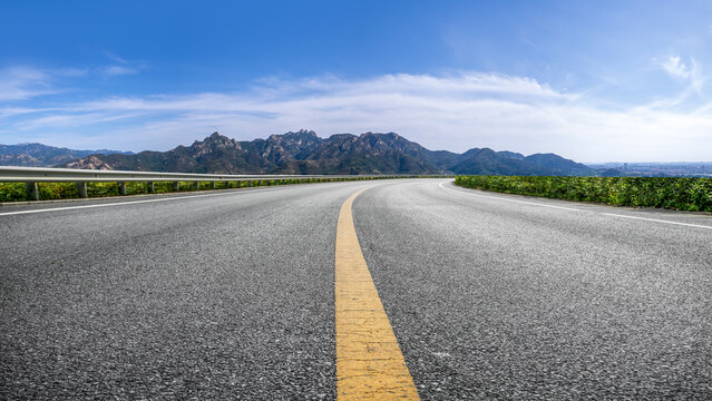 Curved asphalt highway leading to distant mountain ranges under clear blue sky