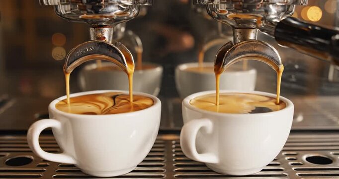 Two espresso shots being brewed simultaneously in a caf?, with blurred background activity