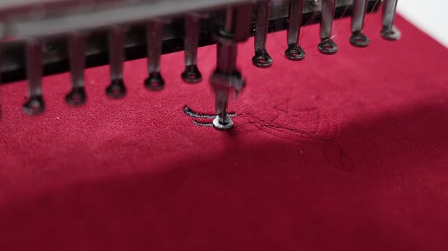 Close-up of an embroidery machine stitching black thread onto red fabric for a traditional Albanian garment, highlighting precision textile craftsmanship.
