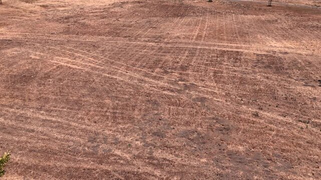Cinematic drone push-in reveal over a drought-stricken public park with dry brown grass and exposed soil during the California summer dry season in San Jose, California. Aerial footage illustrating dr