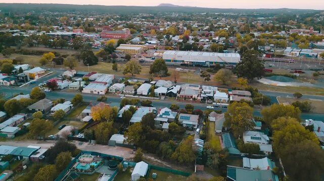 Aerial view of a charming rural town at sunset featuring residential homes, green trees, and distant mountains under a dramatic sky.