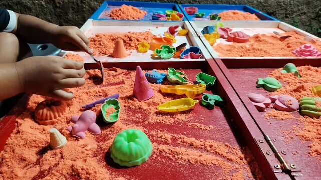 A close-up video showing a child's hands playing with kinetic sand using colorful toys and molds.