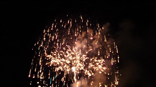 Spectacular golden, red, pink, and white fireworks explode, illuminating dark night sky. Dazzling display of color and light, brilliant, bright celebration with joyous sparkle and wonder